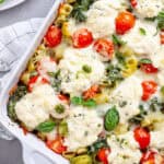 A close up of a baked ricotta pesto pasta topped with tomatoes, spinach and melty cheese.