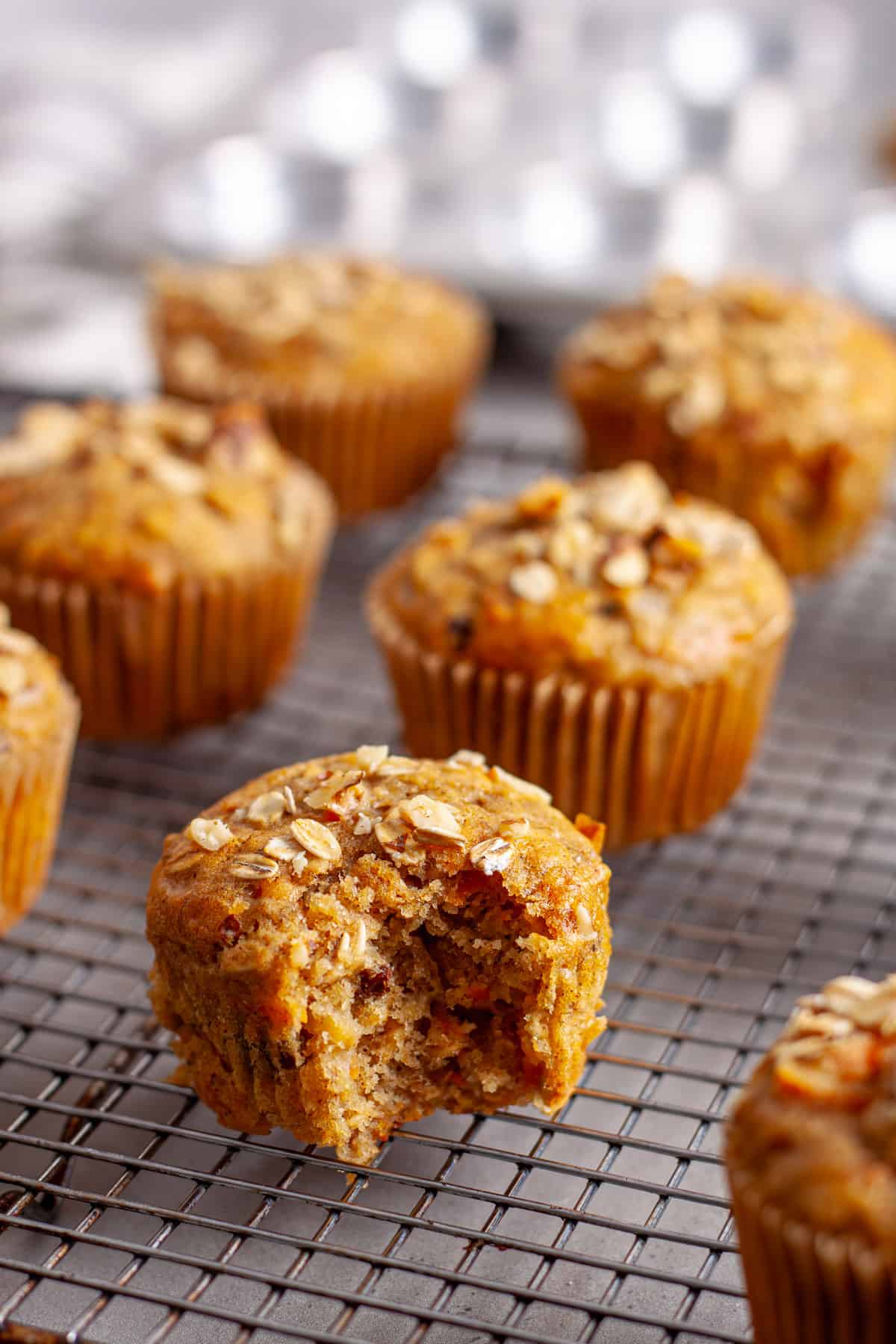 A bite taken out of a carrot banana muffin cooling on a wire rack.