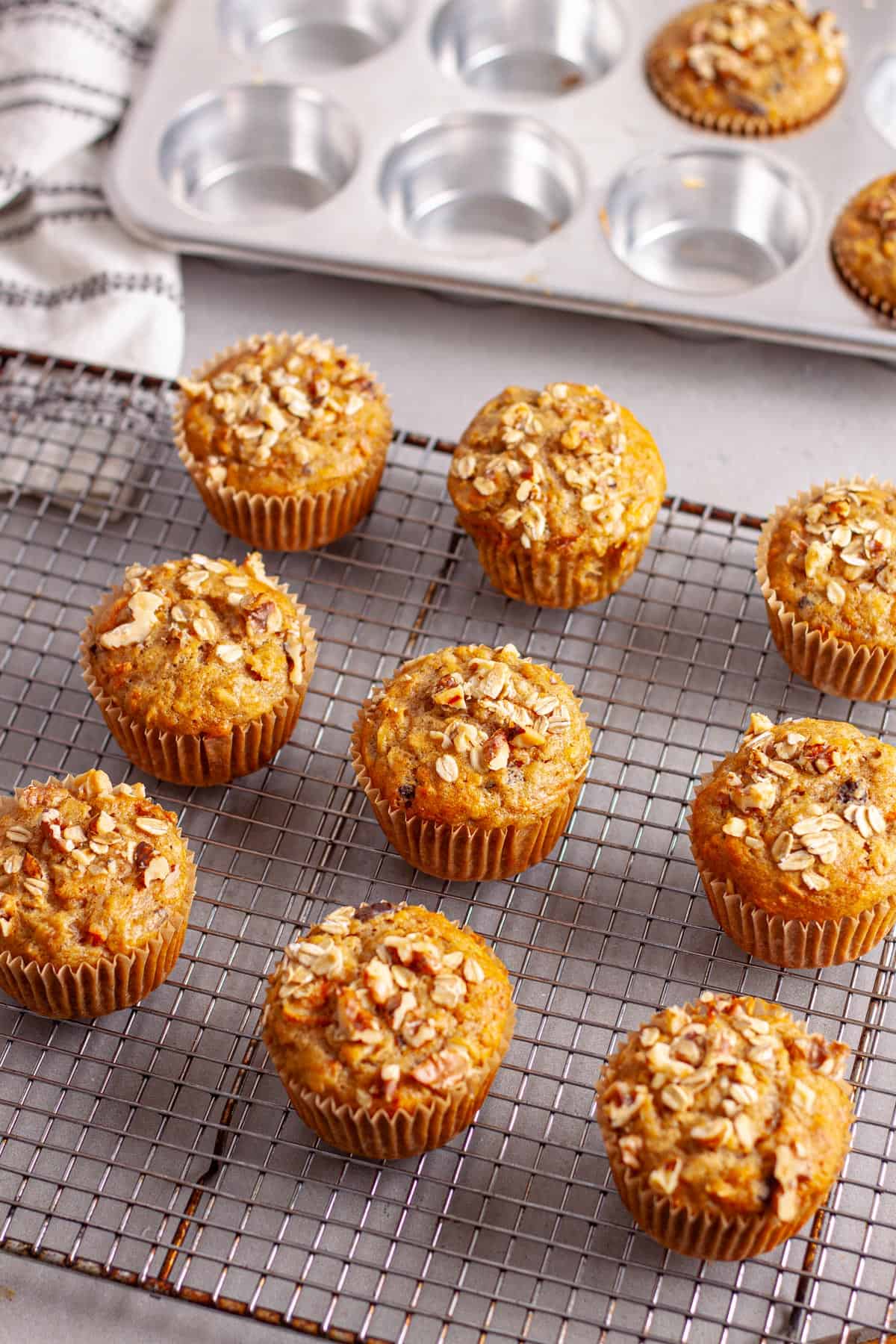 A wire rack with carrot and banana muffins cooling and a muffin tin in the background.