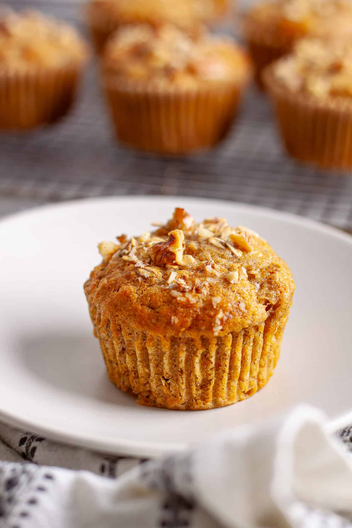 A freshly baked carrot banana muffin on a small plate with the muffin tin in the background.