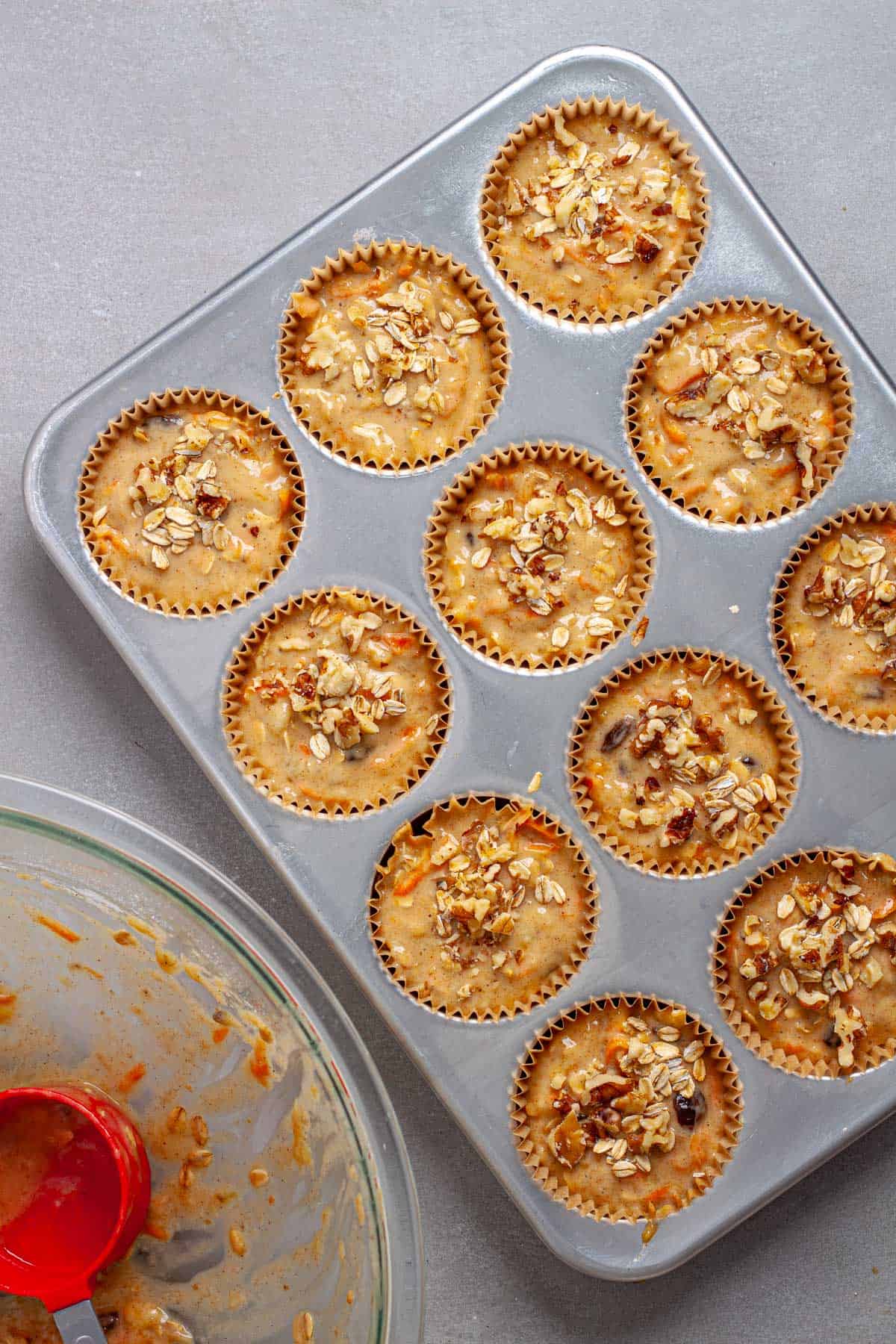 Banana and carrot muffin batter in a muffin tin topped with oats and walnuts.