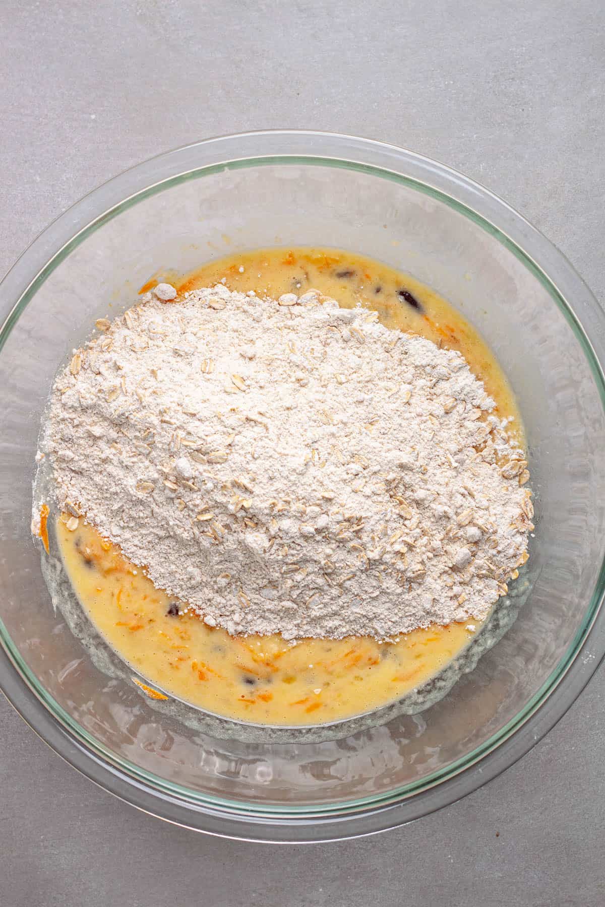 Dry ingredients for muffins added to a mixing bowl with the wet ingredients, including bananas and carrots.