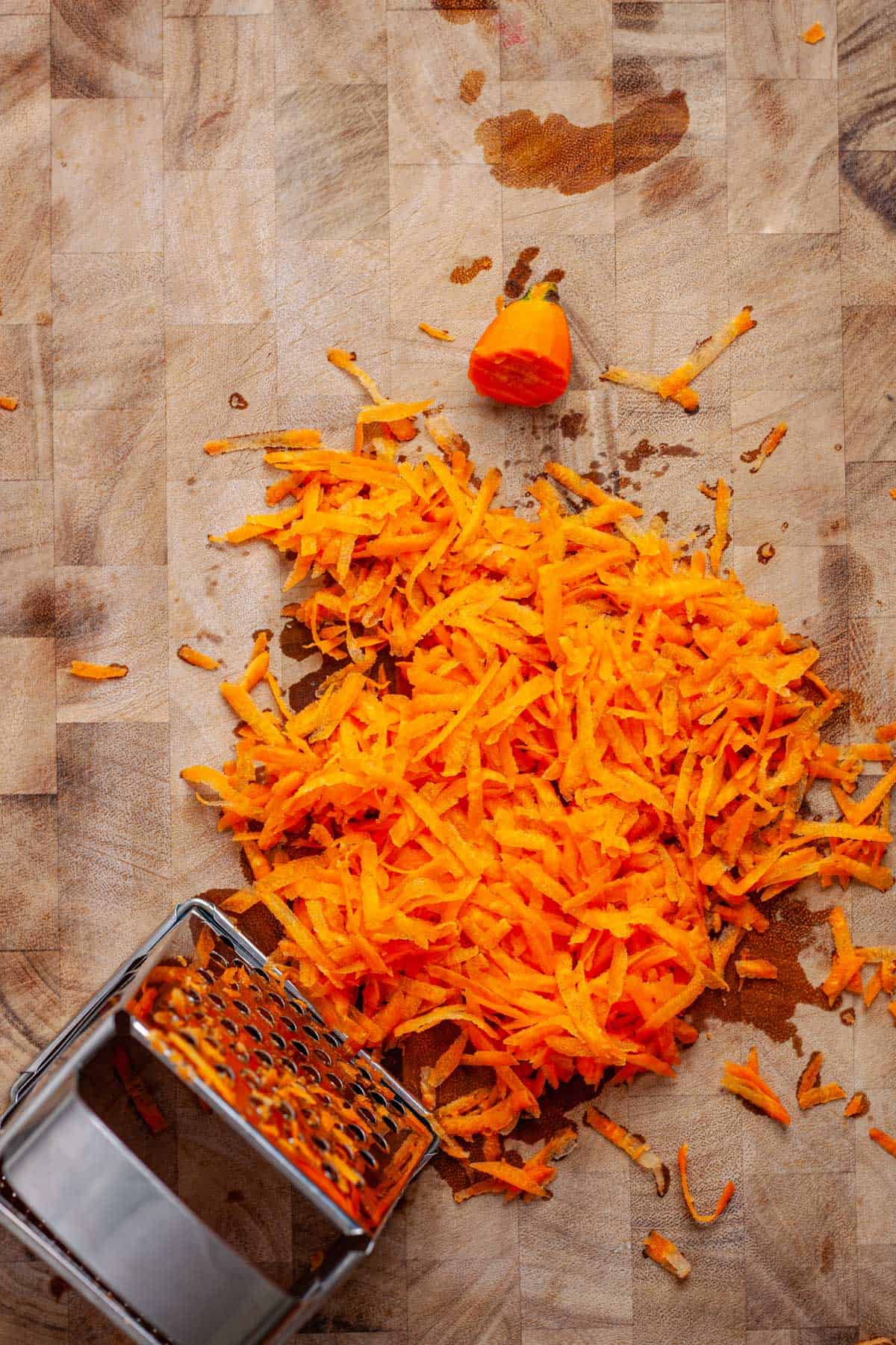 Grated carrots with a box grater on a butcherblock cutting board.