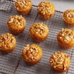 A wire rack with carrot and banana muffins cooling and a muffin tin in the background.