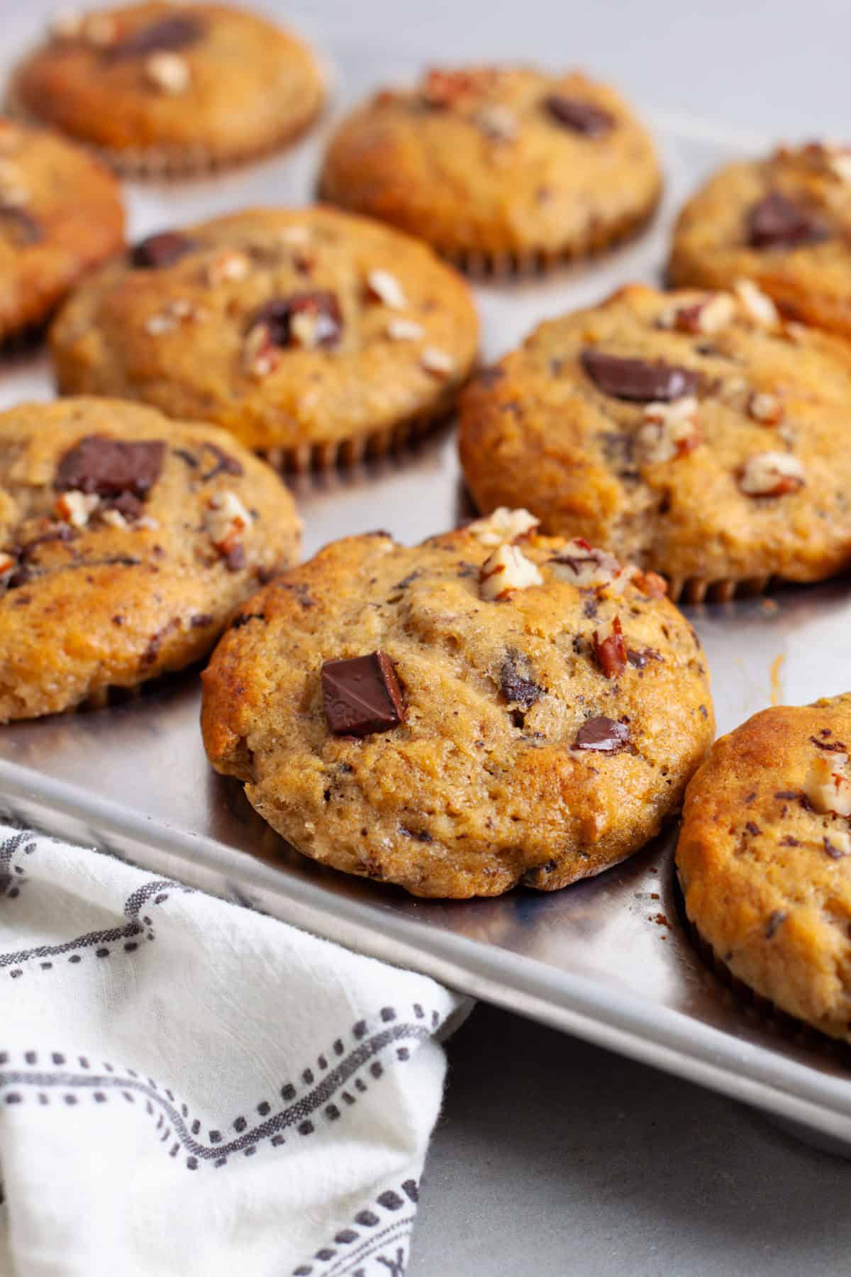 A muffin tin with golden brown banana chocolate chunk muffins on a gray table.