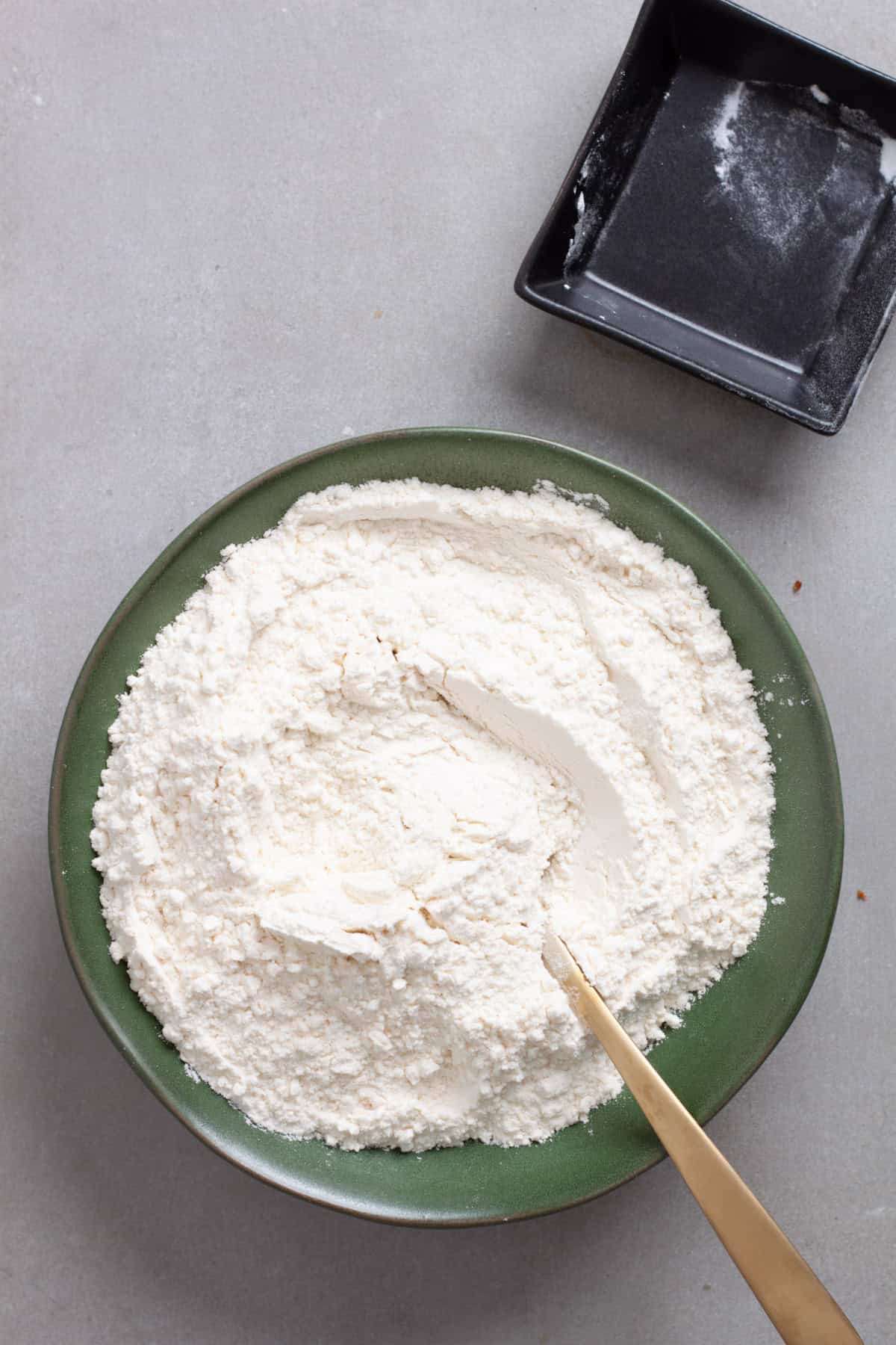 Dry ingredients for banana chocolate chunk muffins getting stirred in a green bowl.