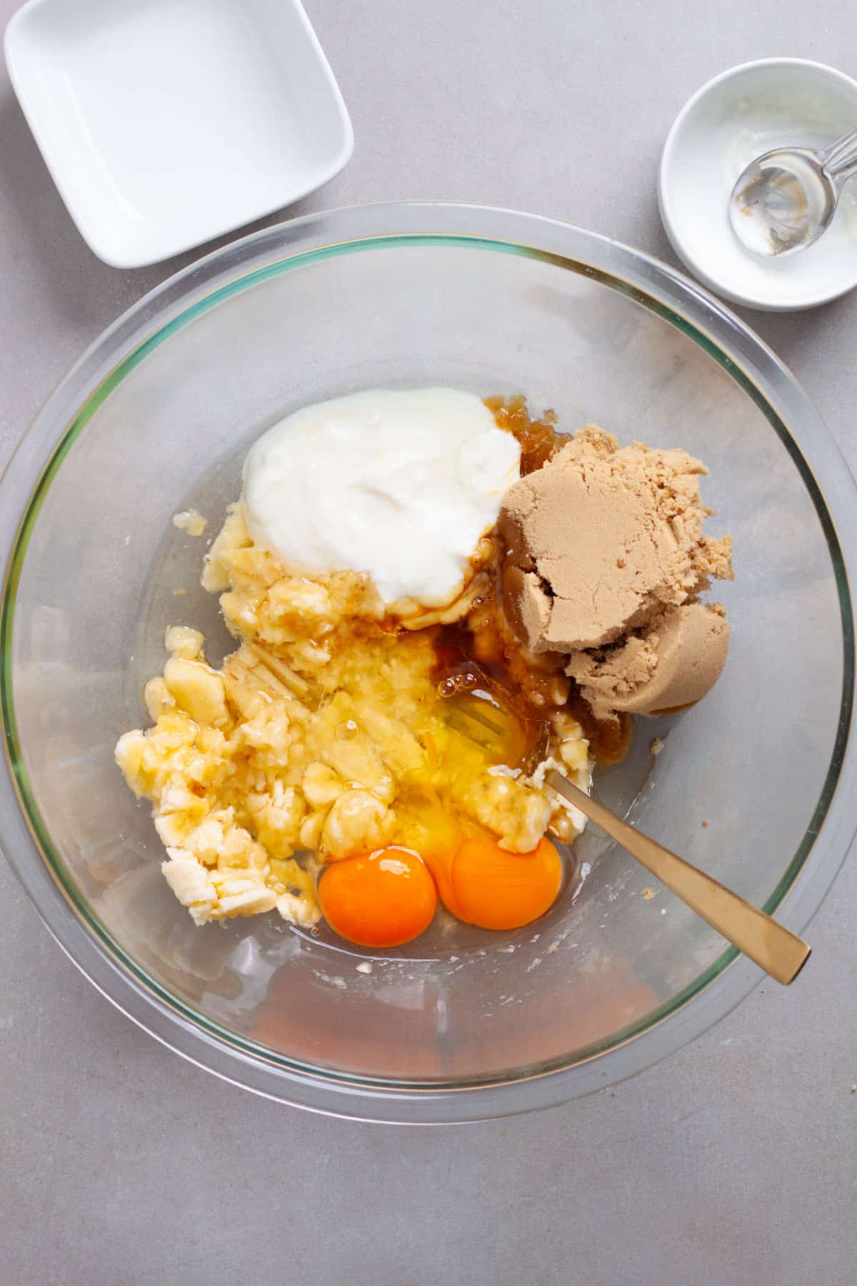 Wet ingredients for banana muffins getting stirred in a glass bowl.