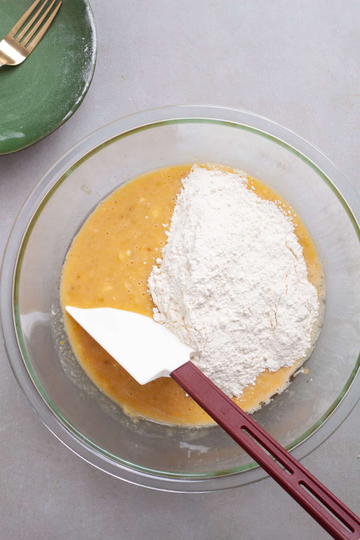 Dry ingredients added to a bowl of wet ingredients for muffin batter in a glass bowl.