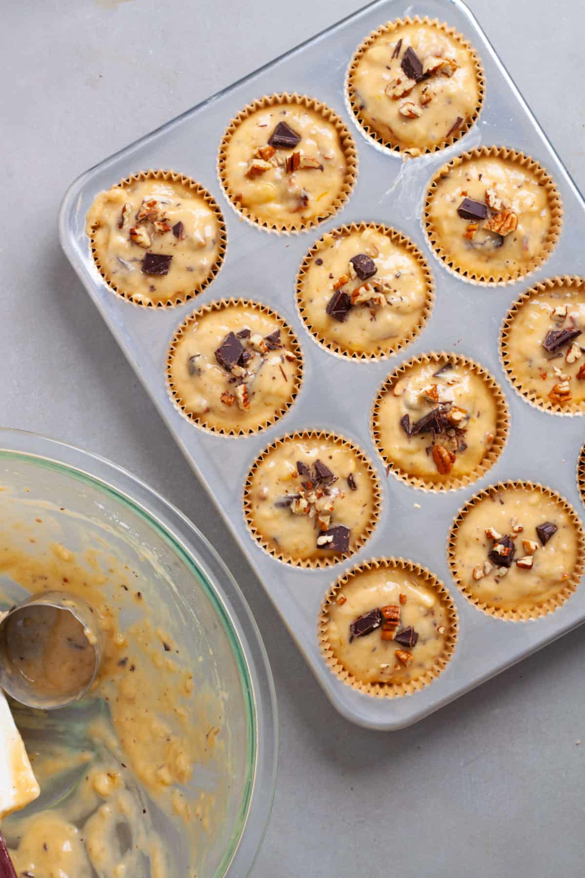 Banana chocolate muffin batter added to a muffin tin and topped with chopped pecans.