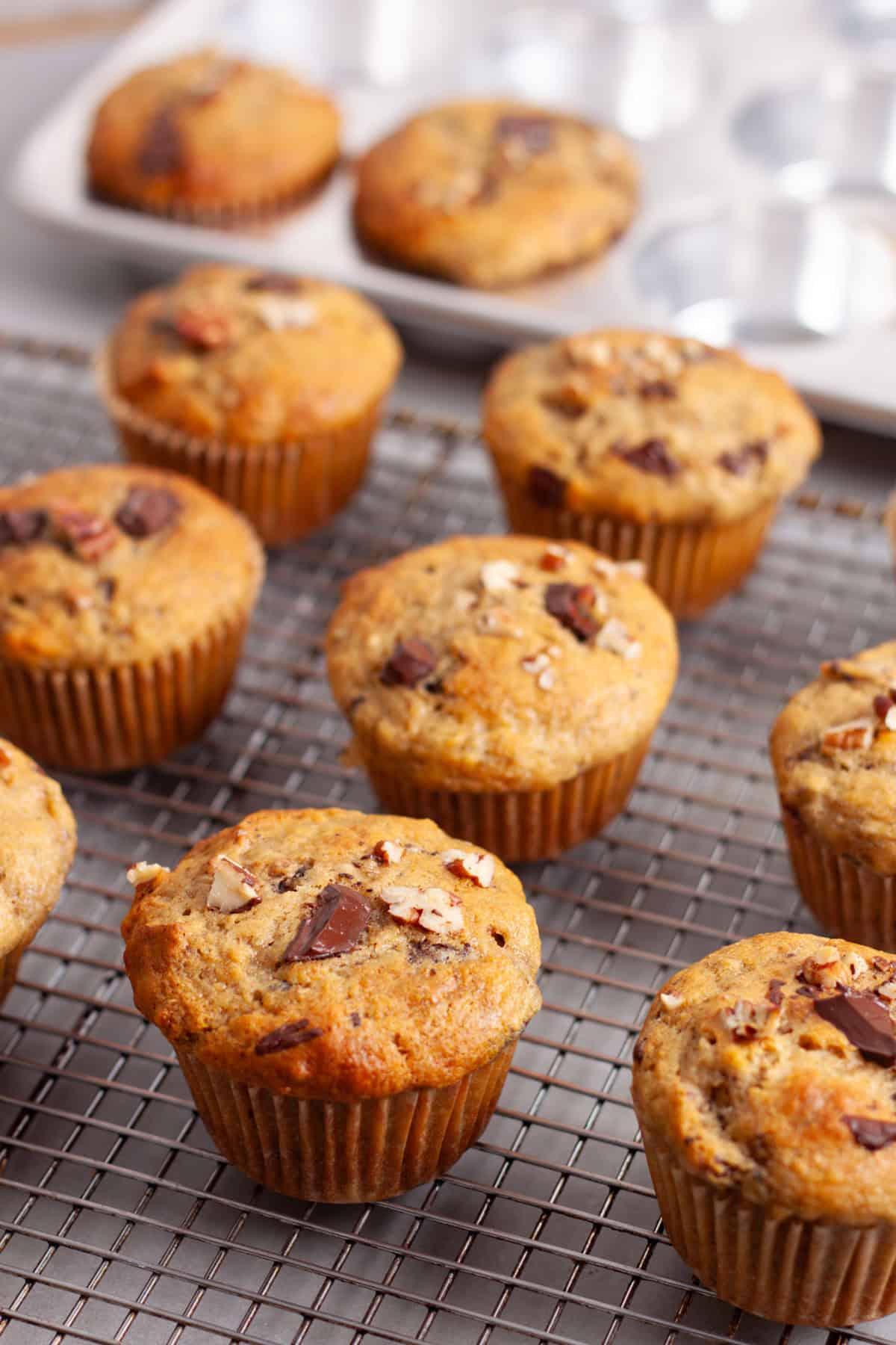 Chocolate chip banana muffins cooling on a wire rack on a gray table.