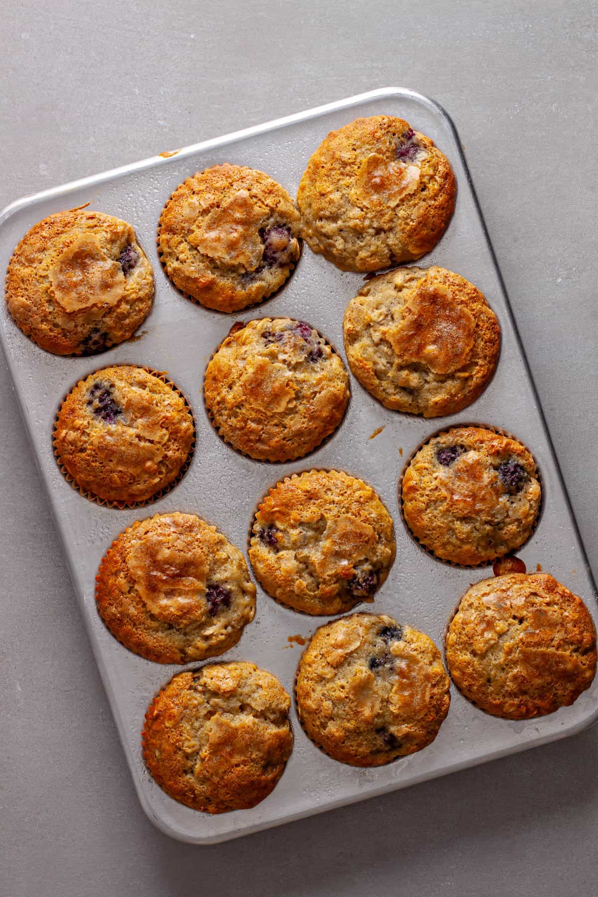 A muffin tin with blackberry banana oat muffins golden brown and fresh out of the oven.