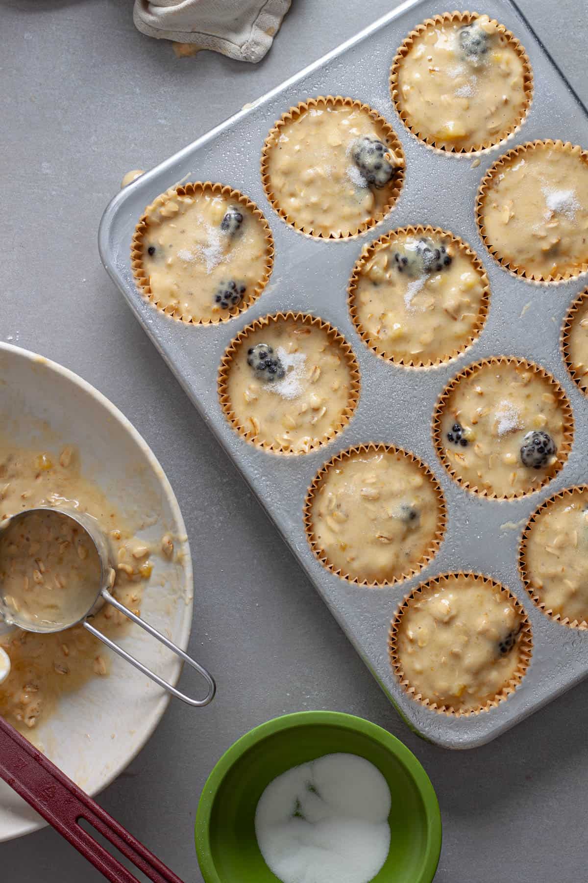 Granulated sugar getting sprinkled onto blackberry banana oat muffins.