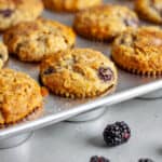 Banana blackberry oatmeal muffins in a muffin tin with loose fresh blackberries in front.
