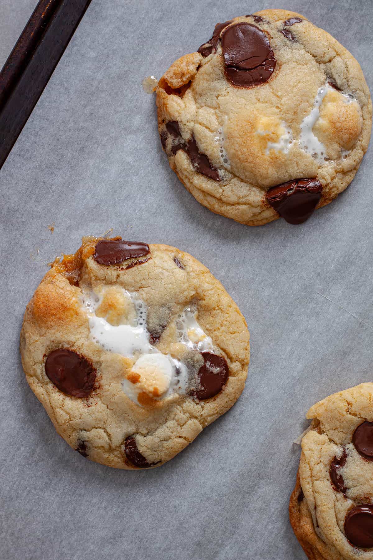 Chocolate chip marshmallow cookies cooling on a parchment lined baking sheet.
