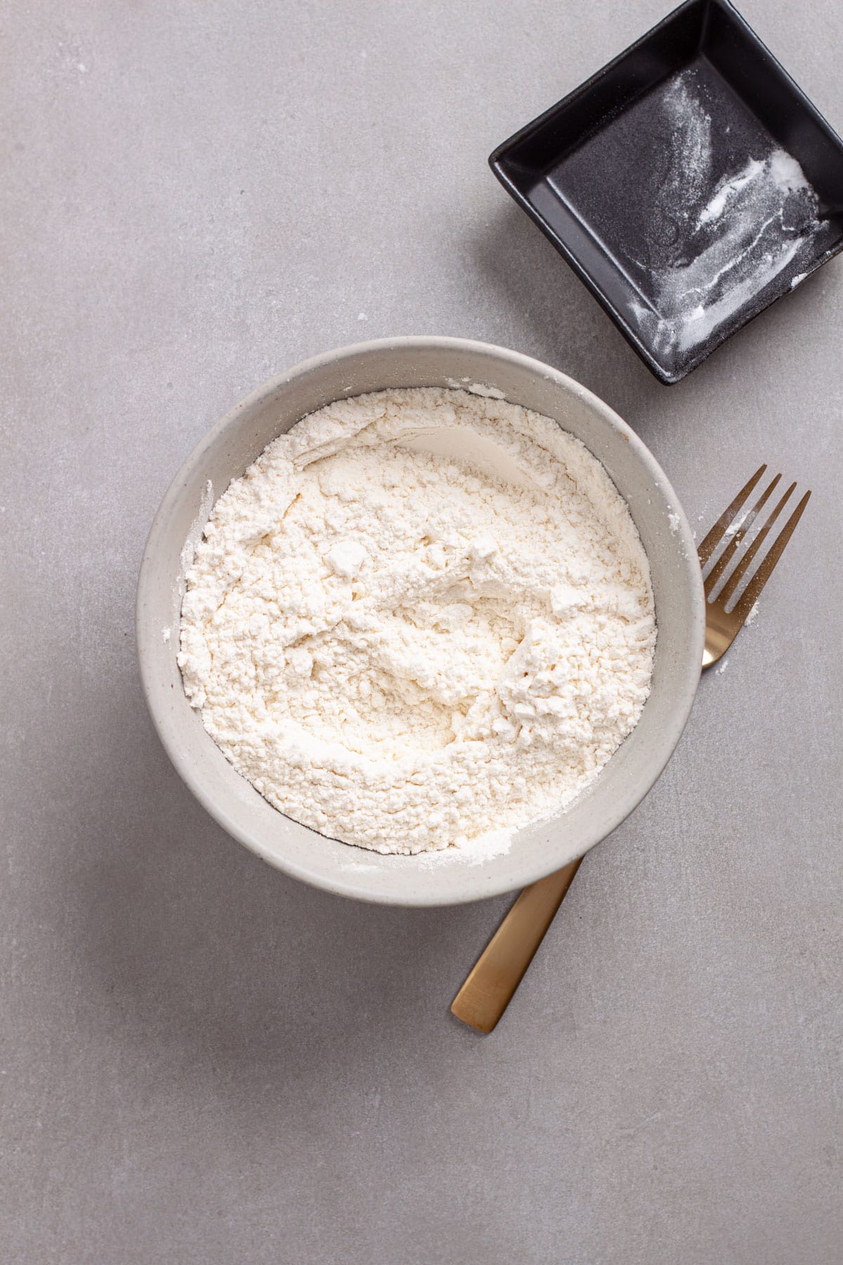 A gray bowl filled with all-purpose flour, baking soda and salt.