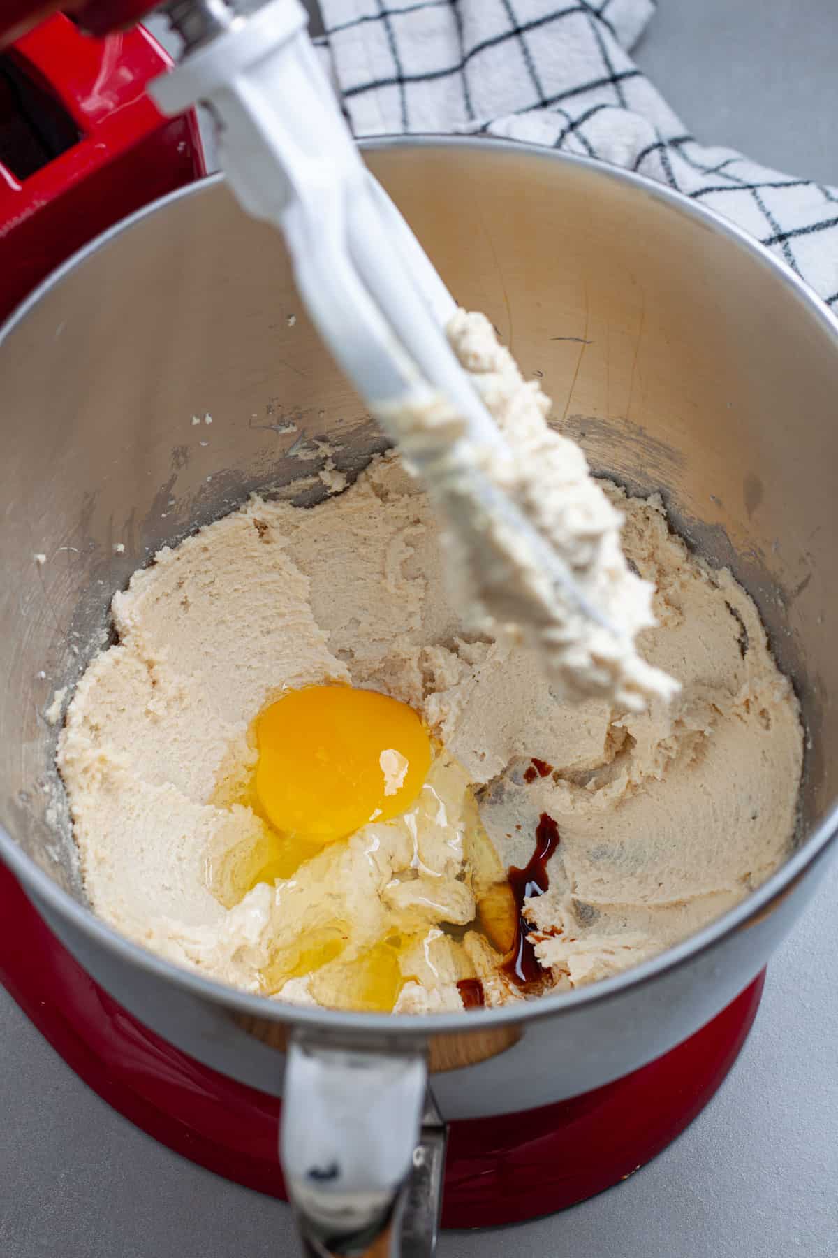 An egg and vanilla extract added to a stand  mixer bowl with whipped sugar and butter.