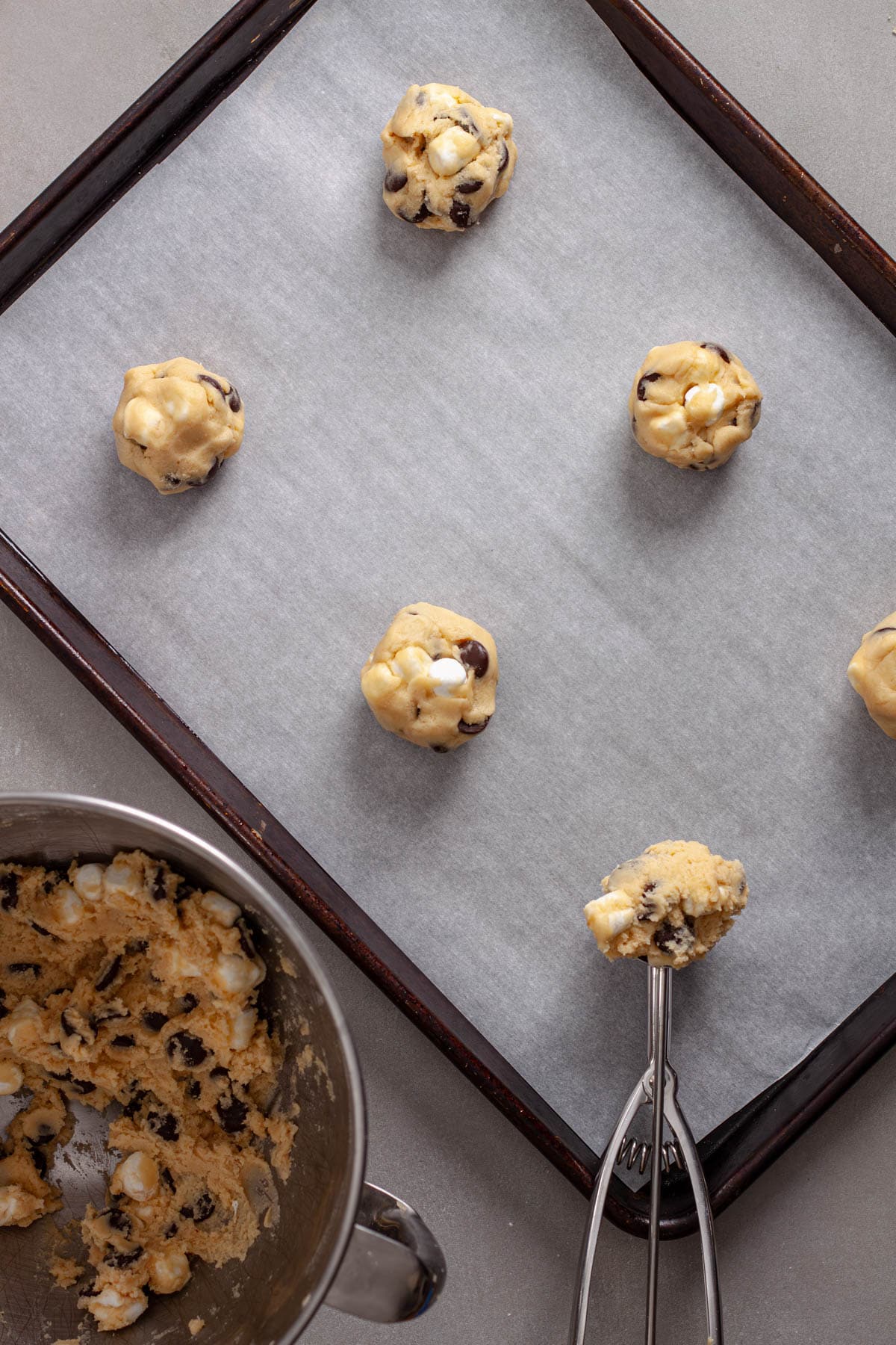 A parchment lined baking sheet with balls of chocolate chips and marshmallow cookie dough.