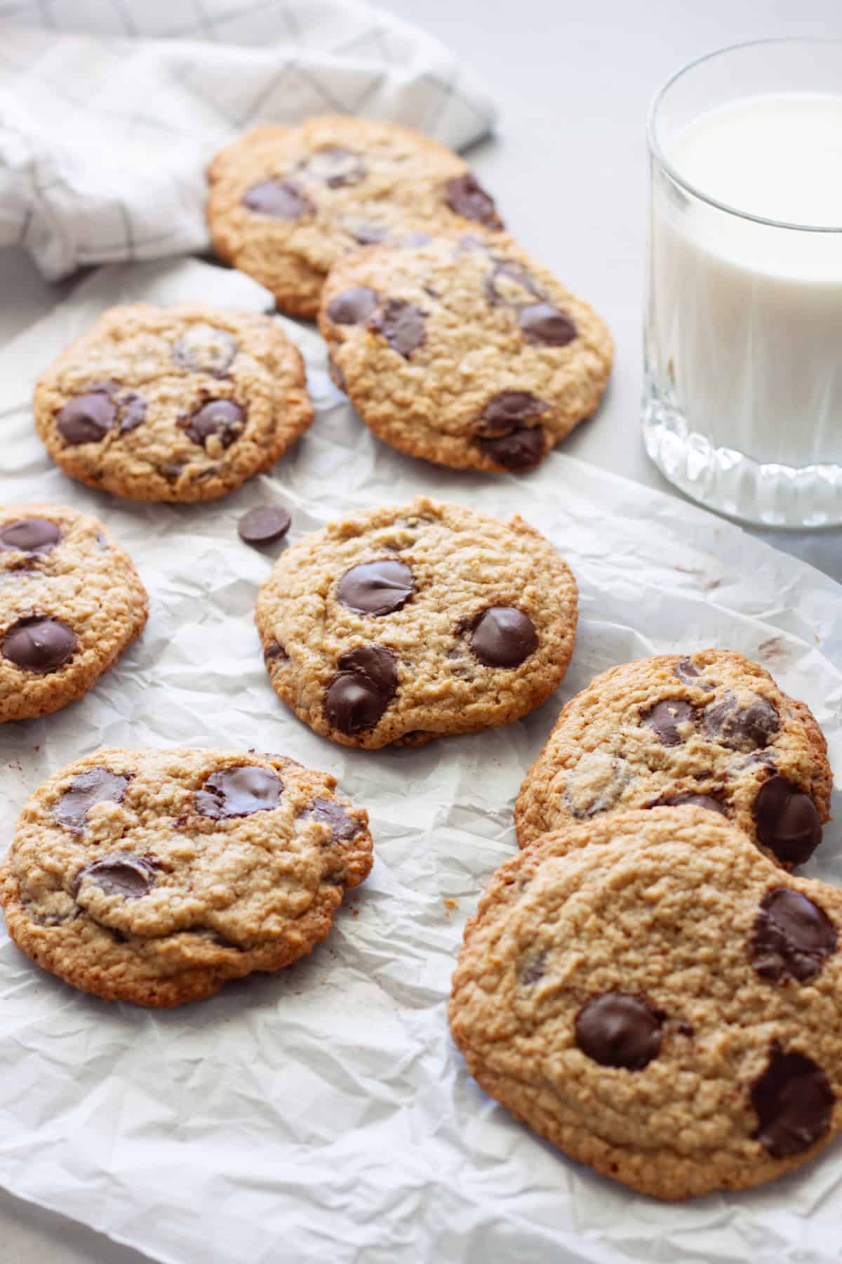 Gluten free chocolate chip cookies on a piece of parchment with a glass of milk to the side.