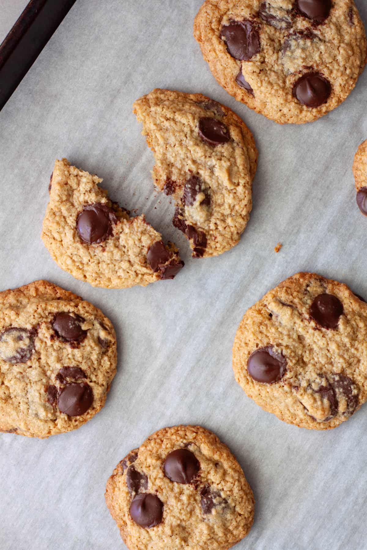A baking sheet with oat flour chocolate chip cookies and one torn in half.