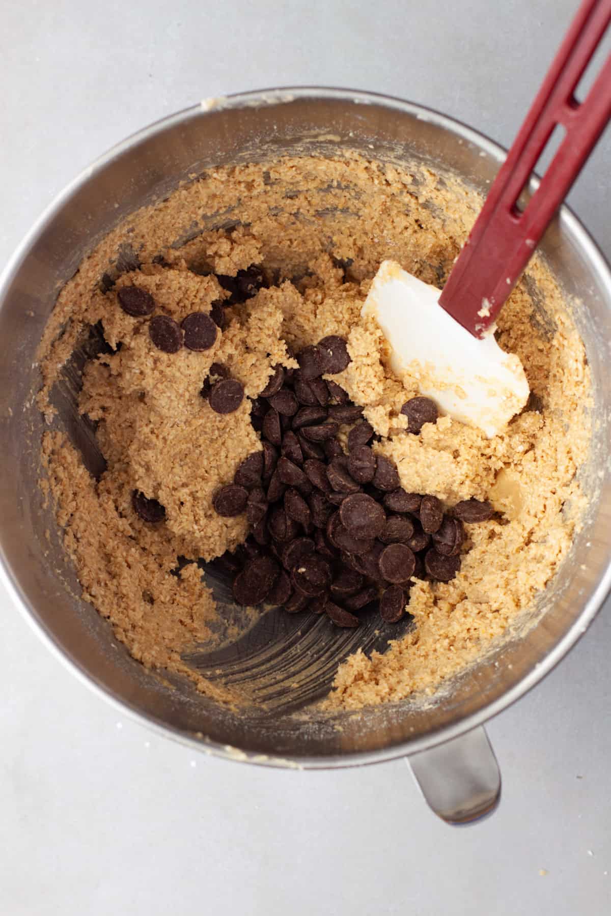 Chocolate chips getting stirred into oat flour cookie dough in a medium bowl.
