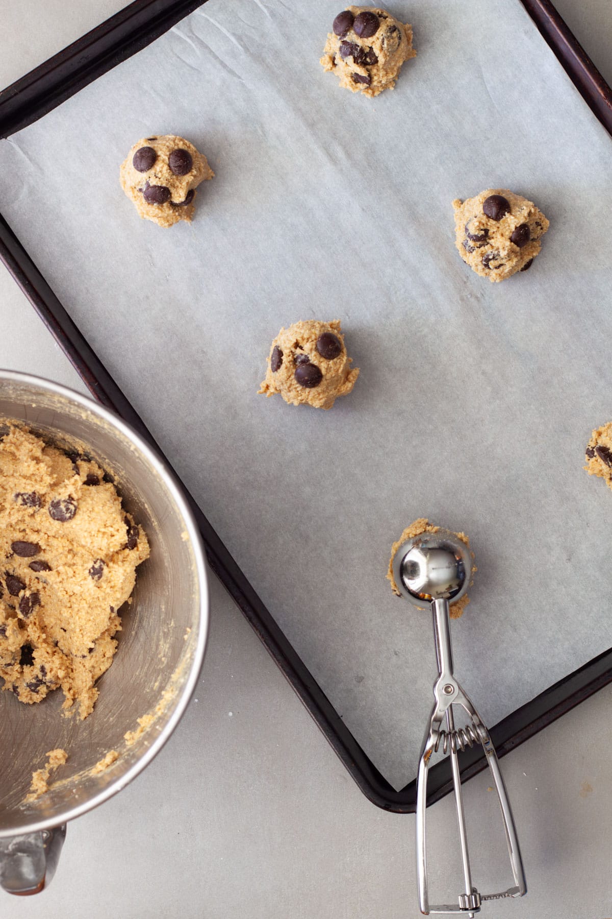 Oat flour chocolate chip cookie dough getting scooped and placed on a parchment lined baking sheet.