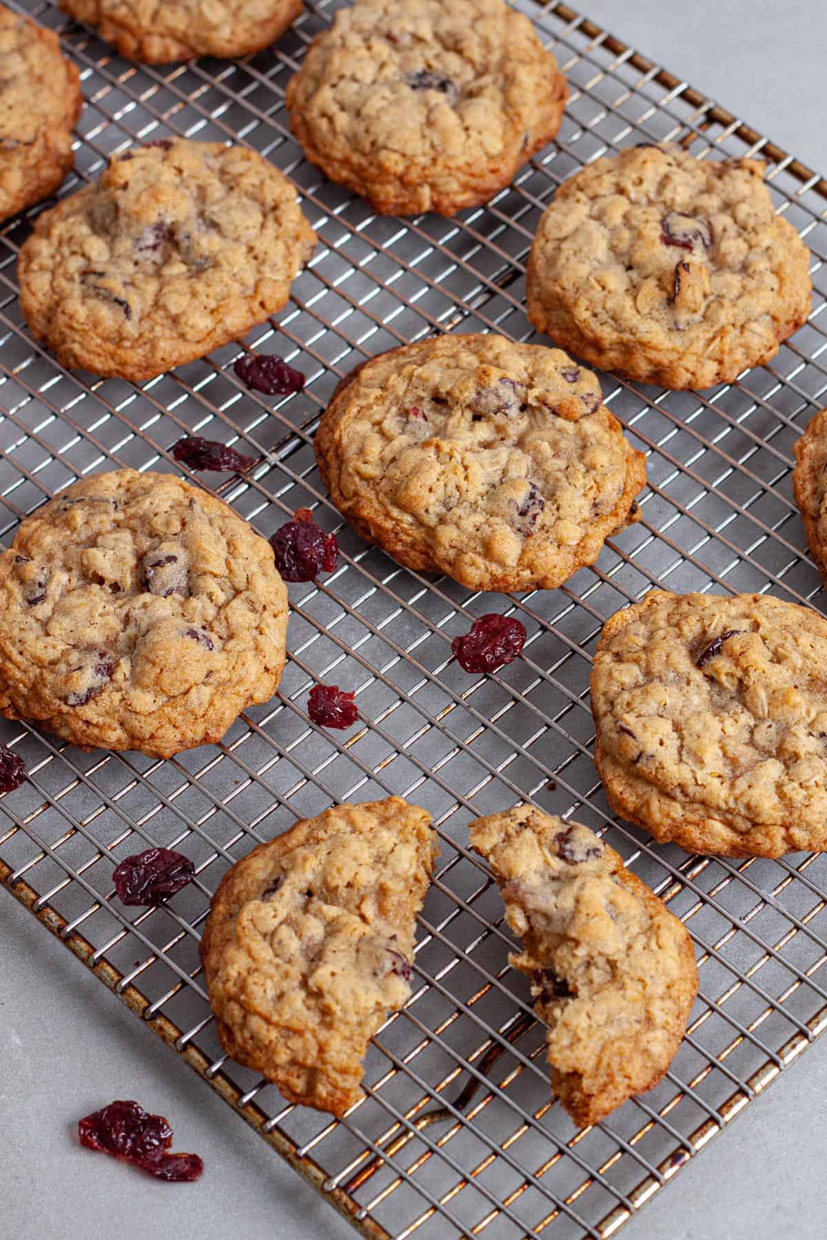 A oatmeal cherry cookie torn in half on a wire rack with more cookies cooling on the rack.