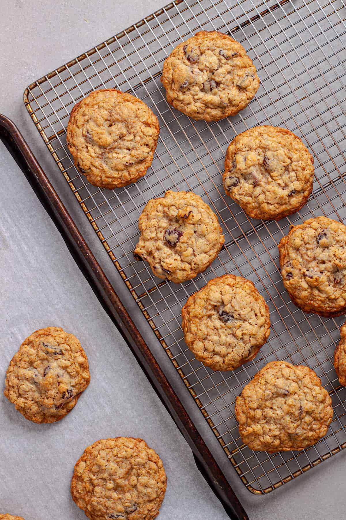 A wire rack with cherry oatmeal cookies cooling and a parchment lined baking sheet to the side.