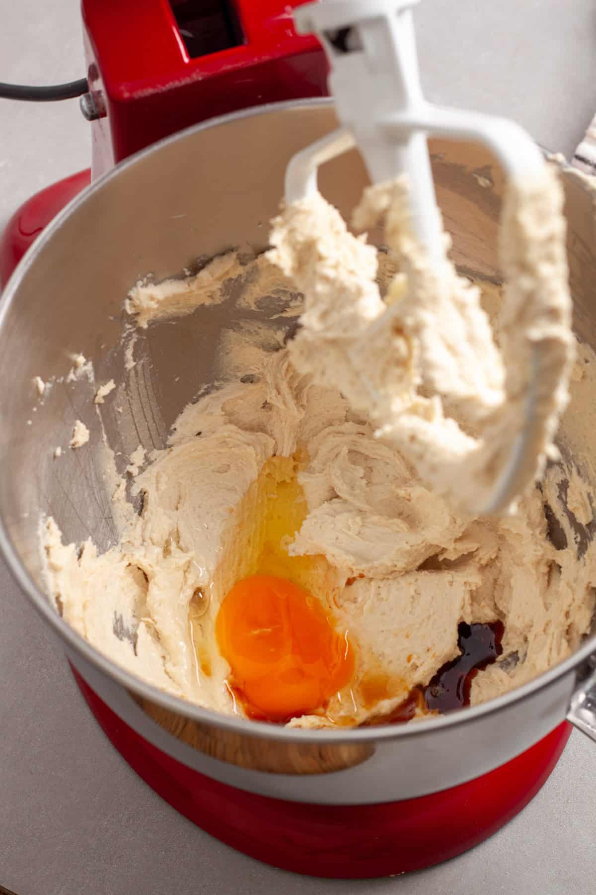 An egg and vanilla added to a stand mixer bowl with whipped butter and sugar.