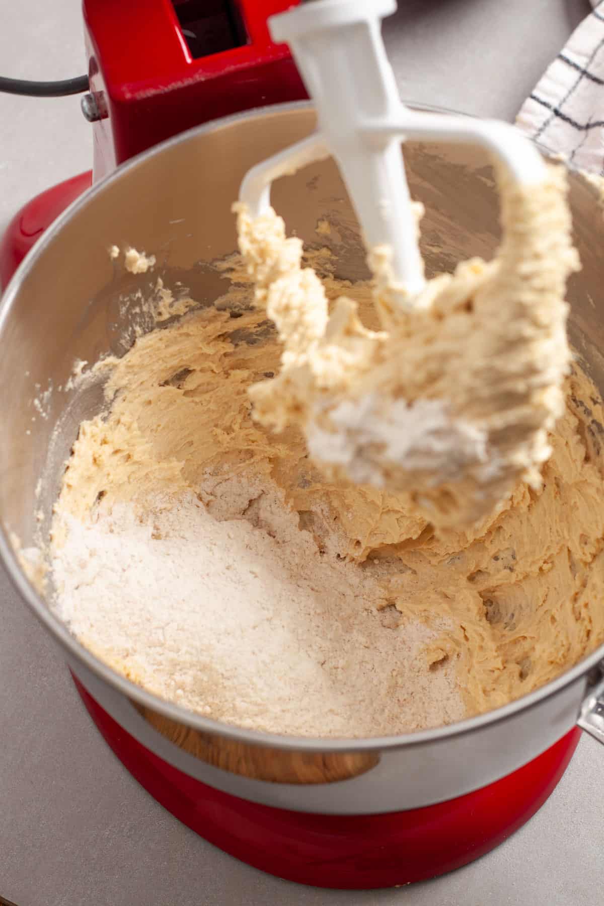 Dry ingredients getting added to a stand mixer with wet ingredients for oatmeal cherry cookies.
