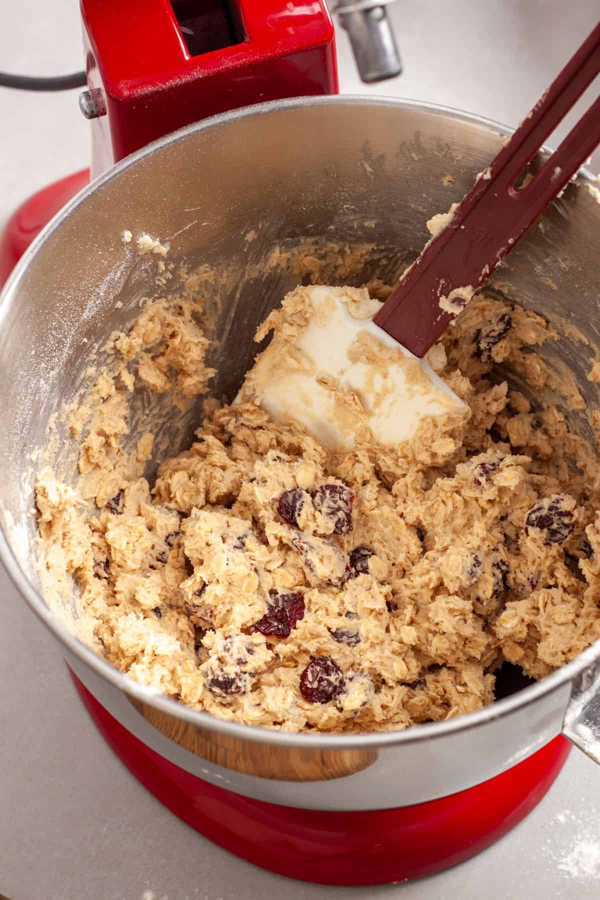 Oatmeal cherry cookie batter getting stirred together by a spatula in a stand mixer.