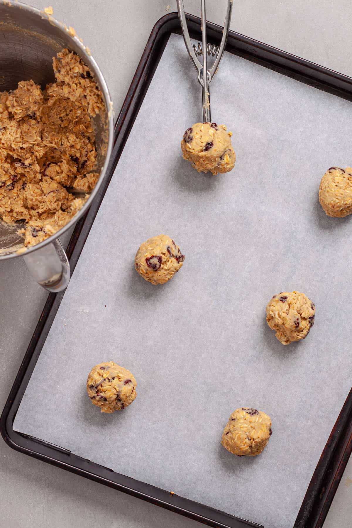 Cherry oatmeal cookie batter portioned out on a parchment-lined baking sheet.