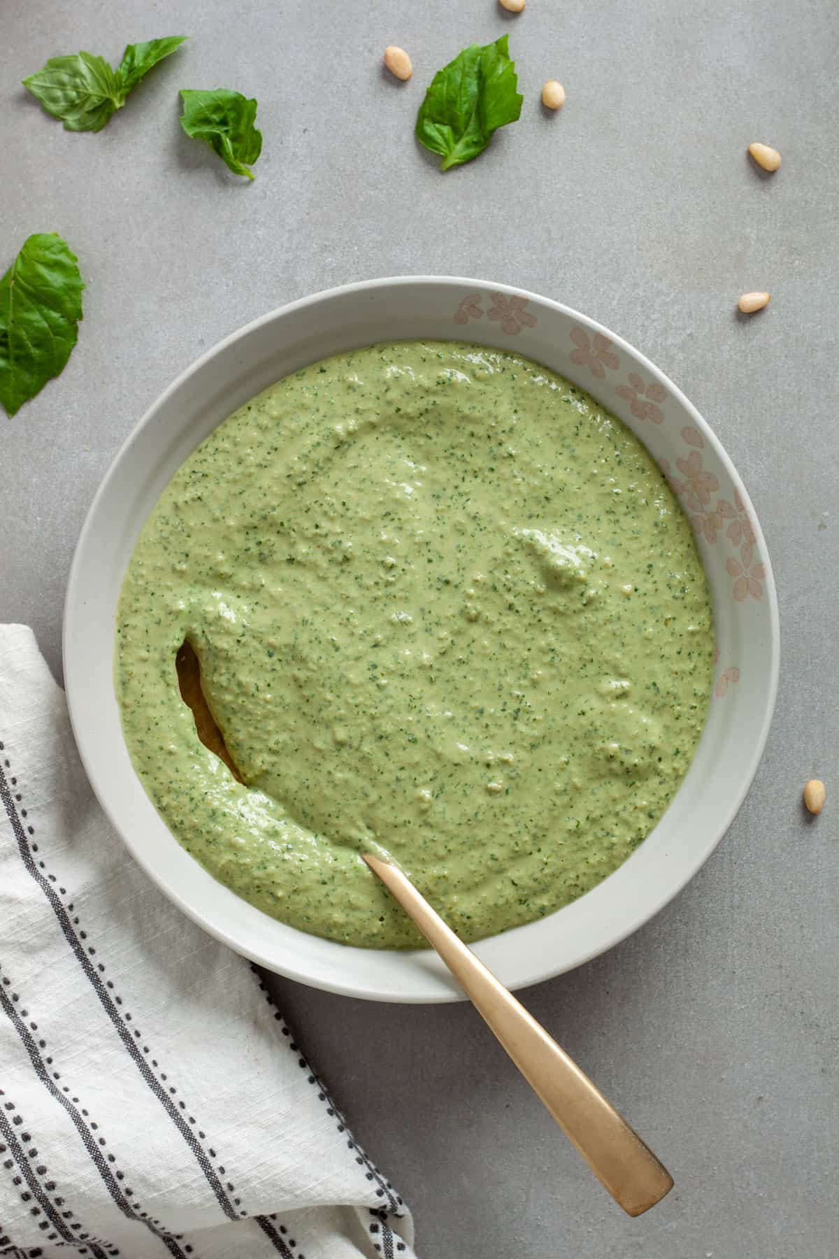 A bowl of ricotta pesto sauce with a gold spoon on a gray table.
