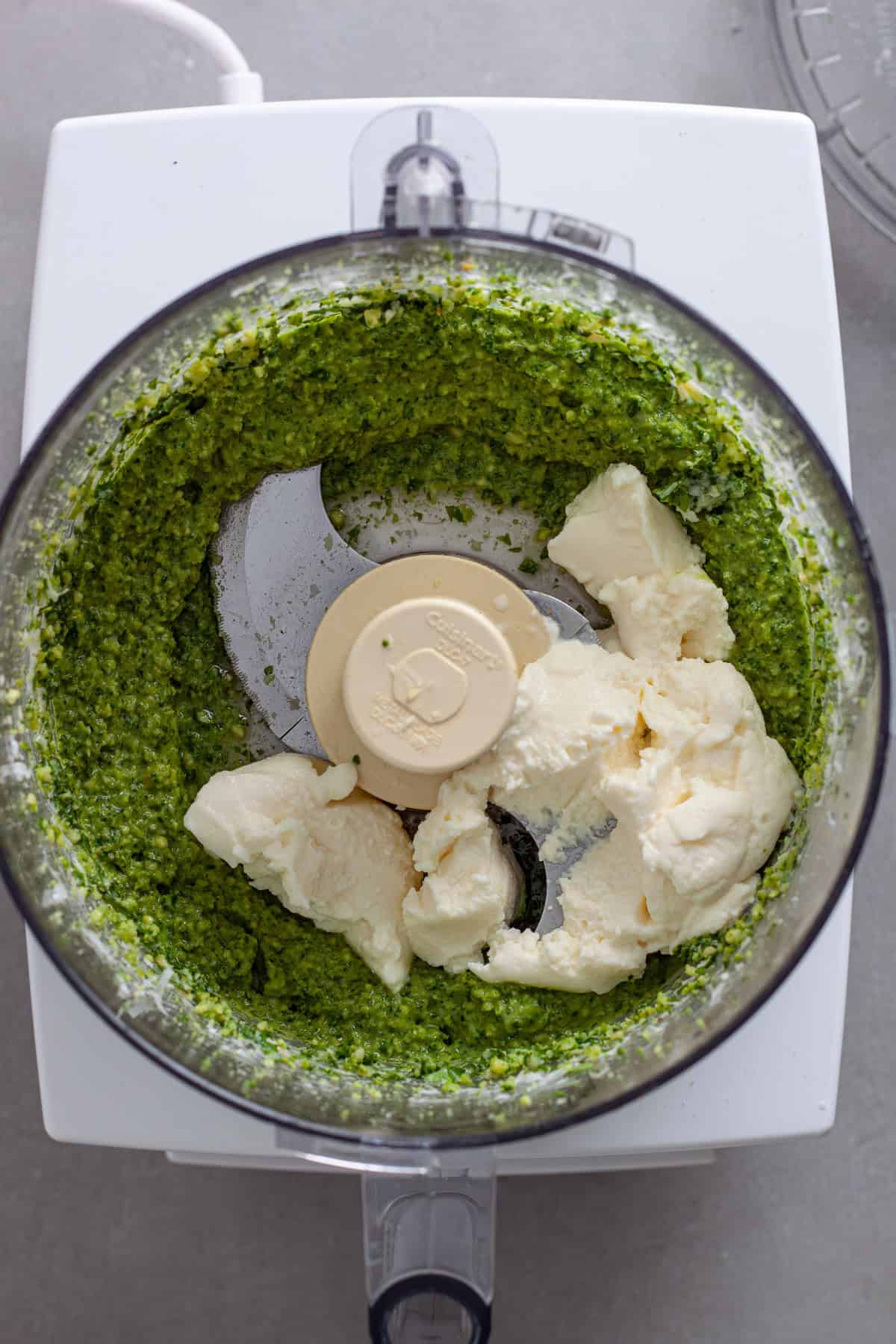 Ricotta cheese added to a food processor with homemade pesto inside.