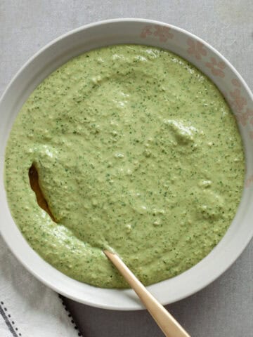 A bowl of ricotta pesto sauce in a bowl on a gray table.