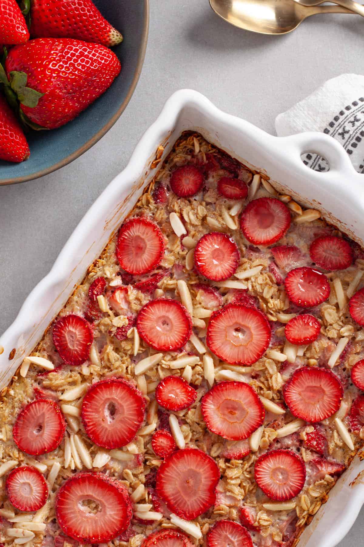 A white baking dish with strawberry and almond baked oatmeal topped with sliced berries.
