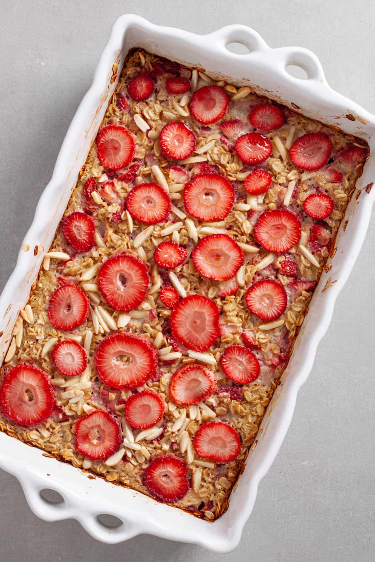 Strawberry and almond baked oatmeal hot out of the oven in a white baking dish on a gray table.