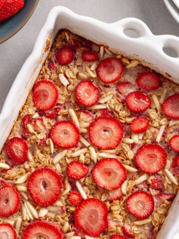 A white baking dish with strawberry and almond baked oatmeal topped with sliced berries.