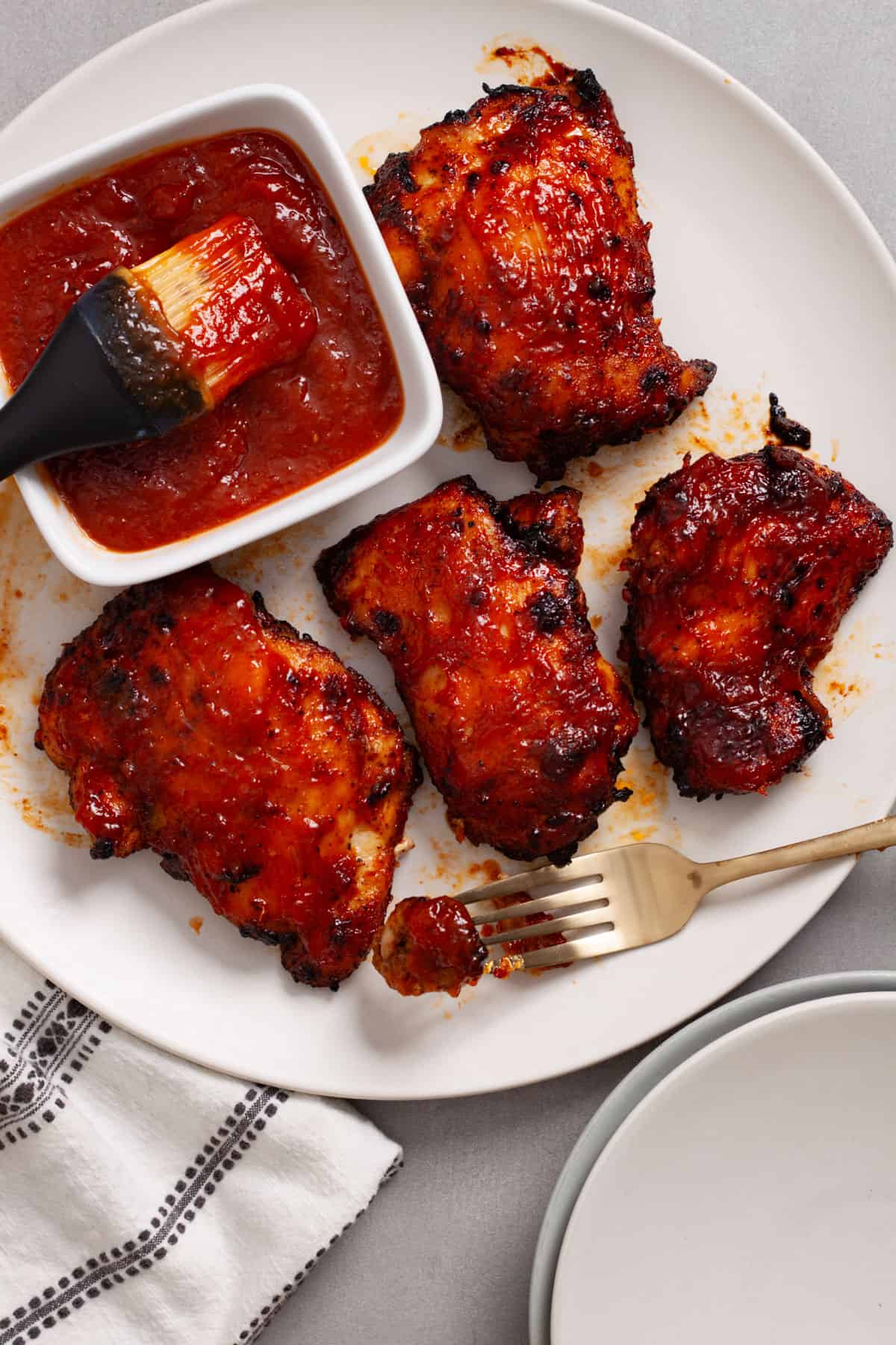 Air fried buffalo chicken thighs on a platter with a small bowl of bbq sauce to the side.