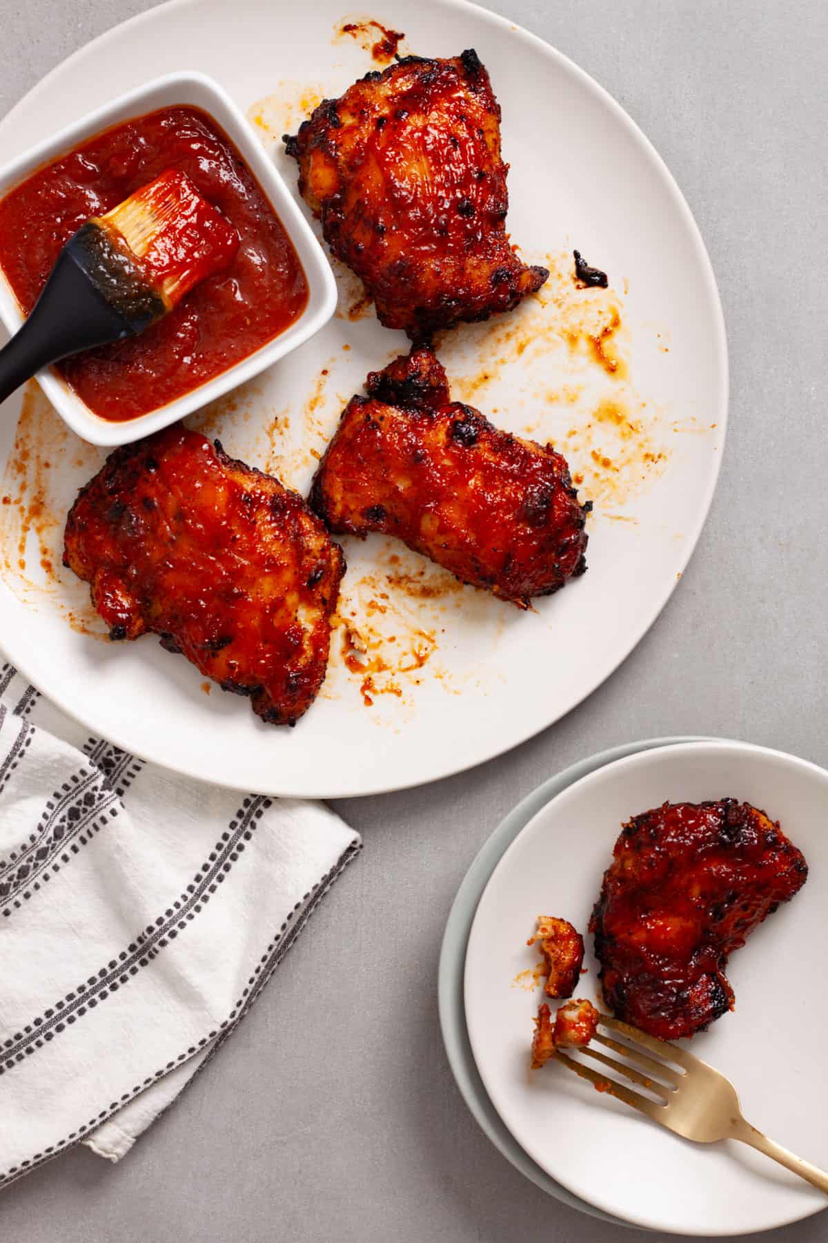 A platter of bbq chicken thighs with a serving off to the side on a small plate.