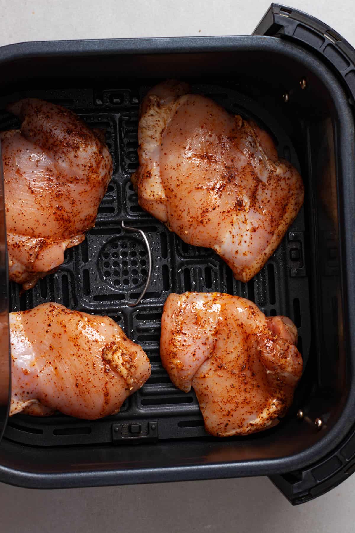 Seasoned raw chicken thighs in the basket of an air fryer.