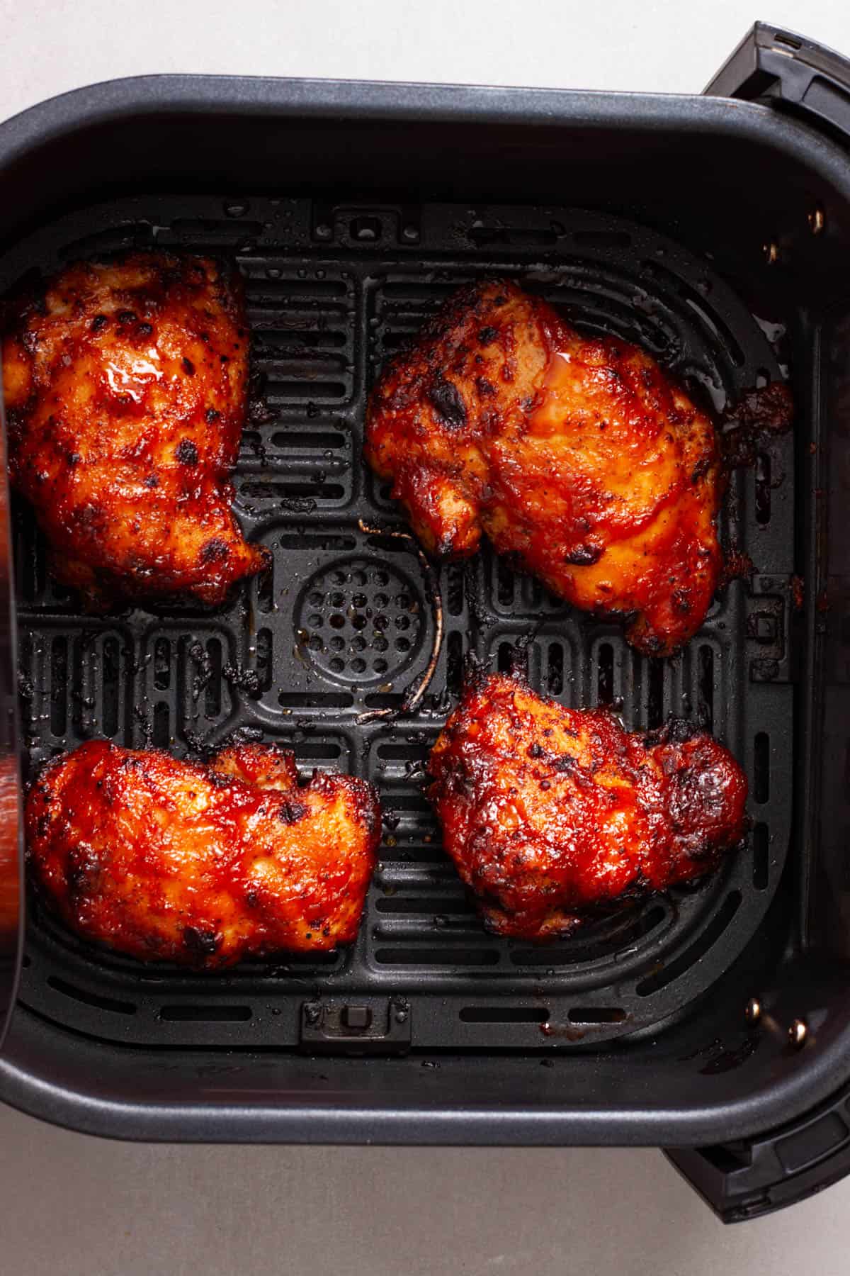Chicken thighs smothered in bbq sauce in a the basket of an air fryer.
