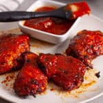 A platter of air fried buffalo chicken thighs with bbq sauce in a small bowl in the background.