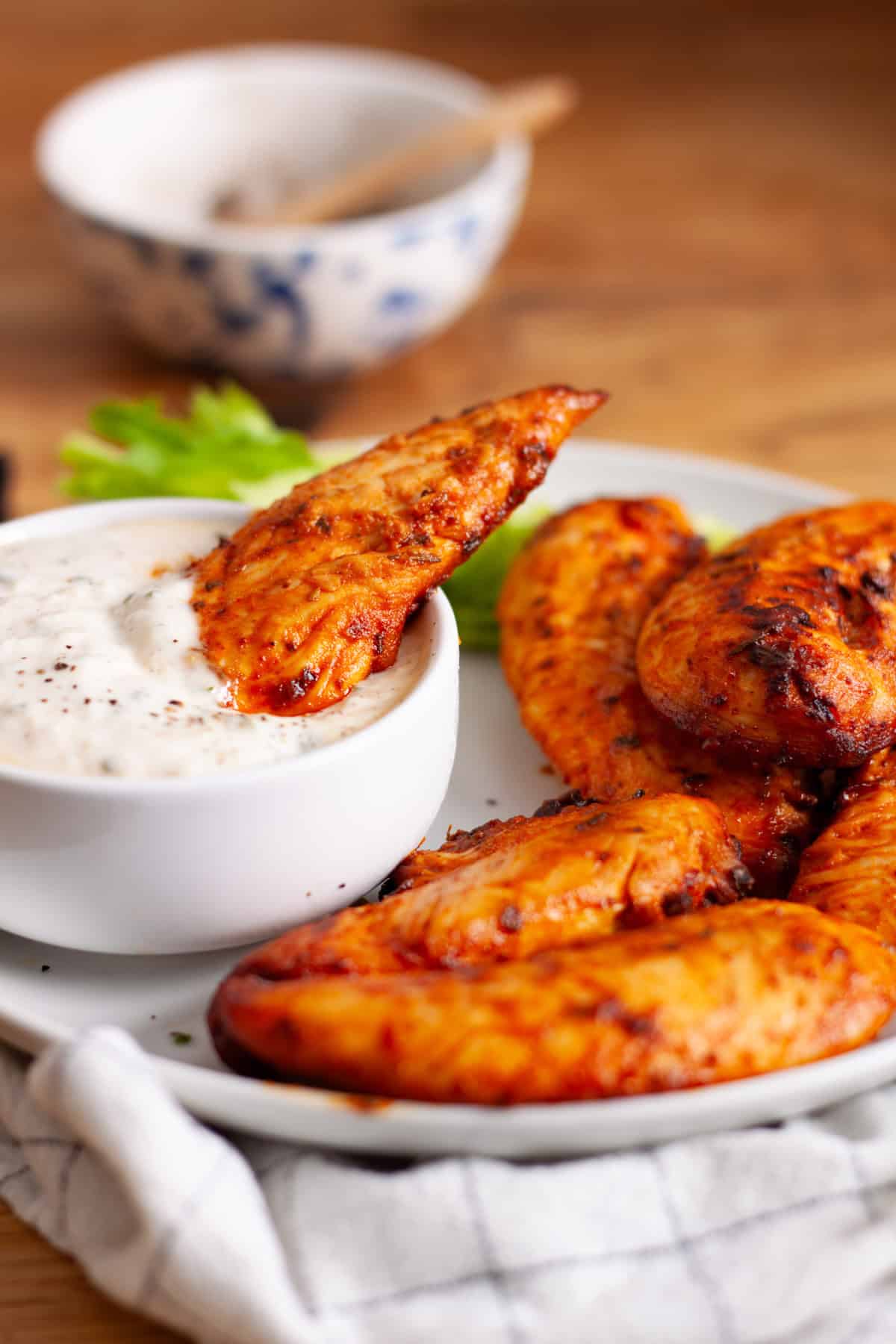 Air fried buffalo chicken tenders in a platter with one dipped into a sauce.