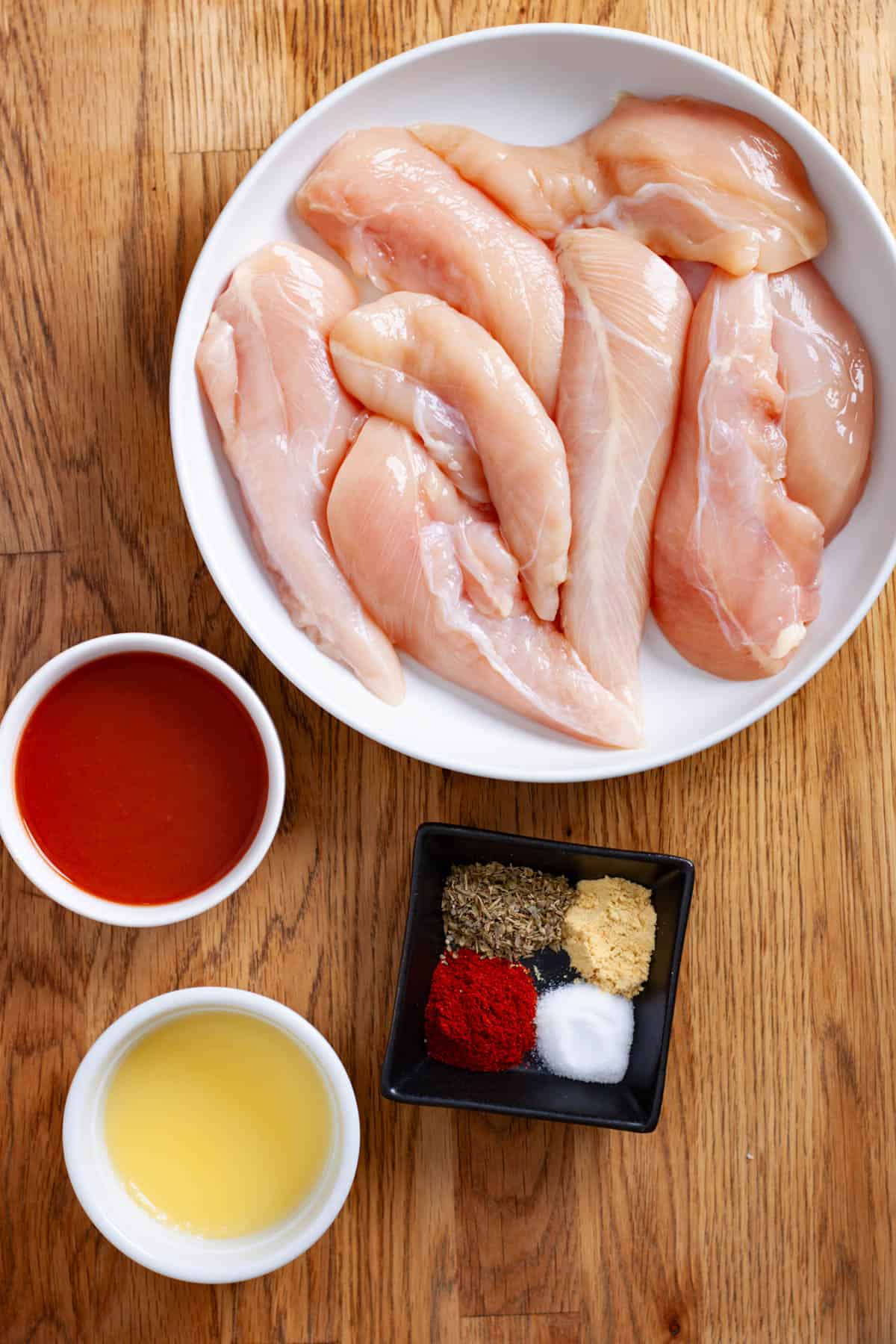 Ingredients for homemade buffalo chicken tender in an air fryer on a butcherblock cutting board.