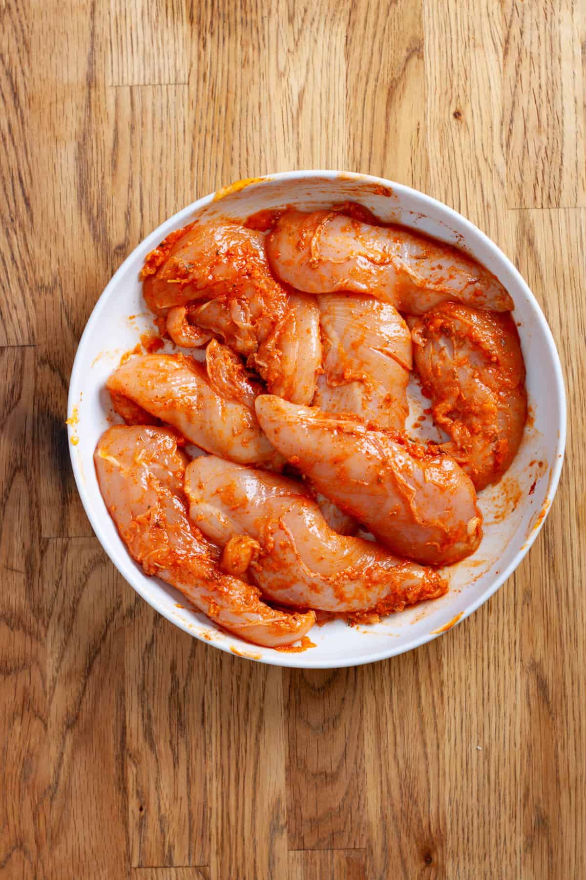 Chicken tenders in a medium bowl marinating with spices and hot sauce.