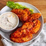 A platter or air fried buffalo chicken strips with a dip and celery to the side.