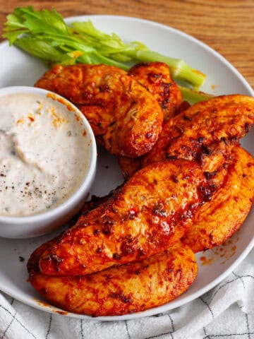 A platter or air fried buffalo chicken strips with a dip and celery to the side.