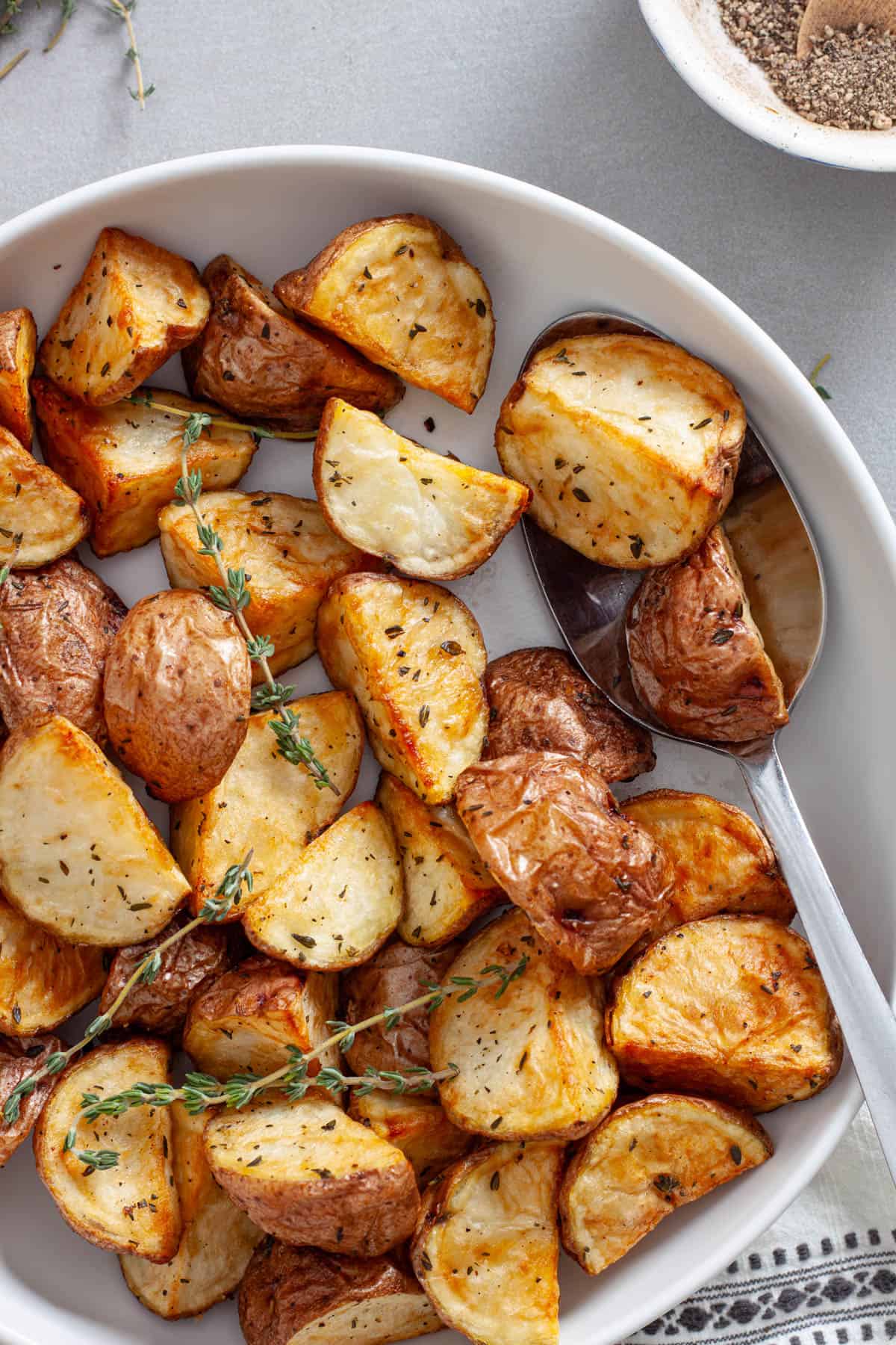 A close up of a bowl of crispy air frier red potatoes garnished with fresh thyme.