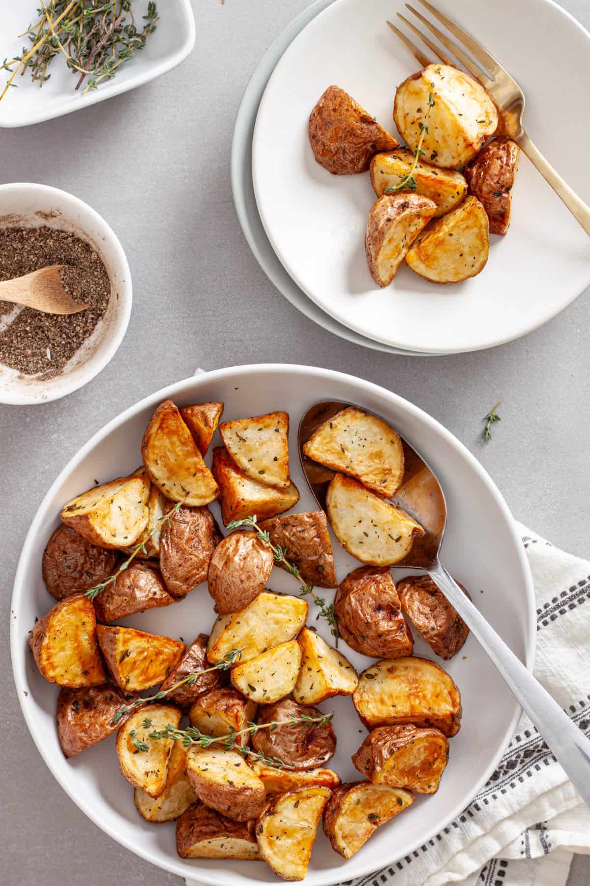 A bowl of crispy air fried red potatoes with a small plate of more potatoes to the side.