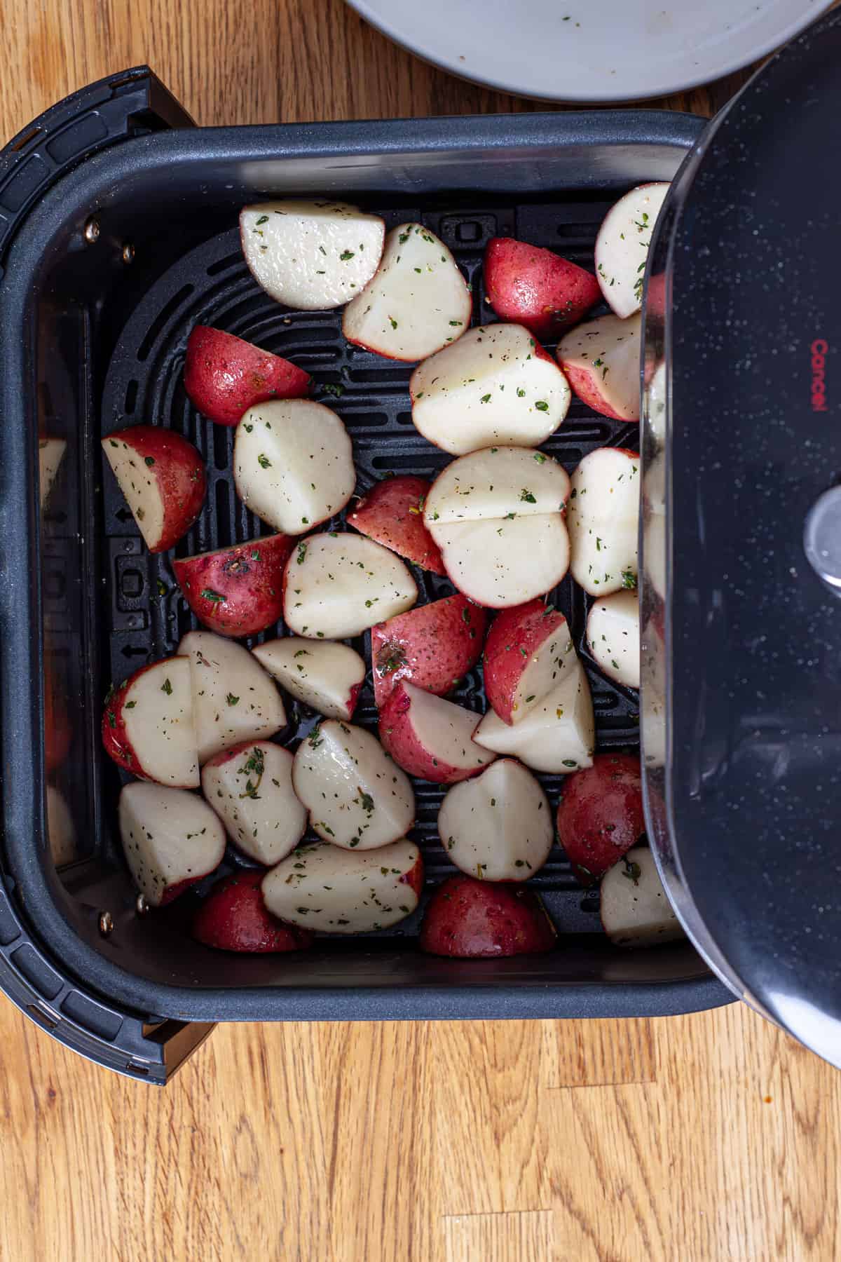 A basket of an air fryer filled with chopped seasoned red potatoes.